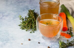 Two glass jars of brown bone broth. Herbs sitting next to them.