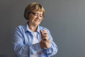 Elderly woman suffering from pain in hand, close up on gray background